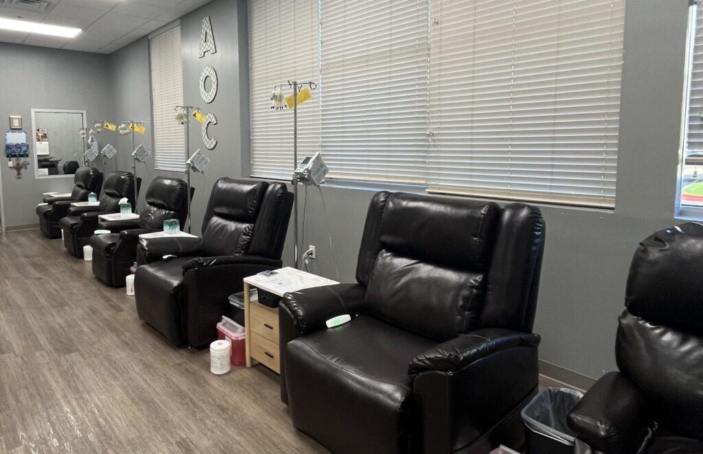 Row of reclining infusion chairs with IV stands and side tables in the AOCBV Infusion Suite.